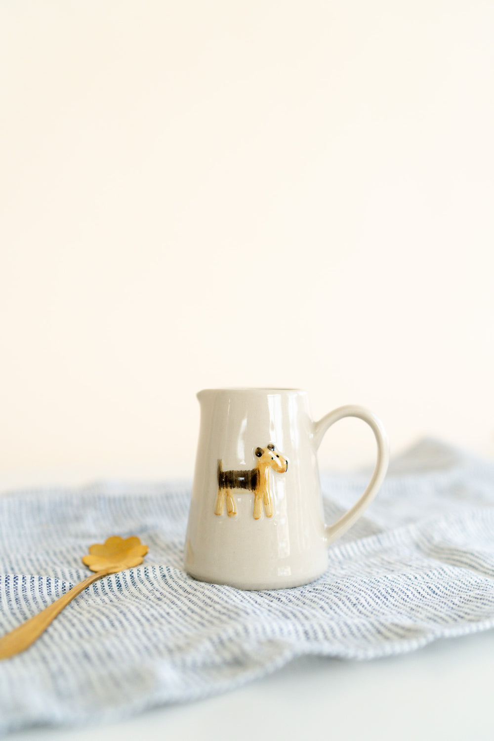 Dog Mini Creamer Pitcher - A petite pitcher with a painted brown dog sits on a striped towel next to a gold spoon